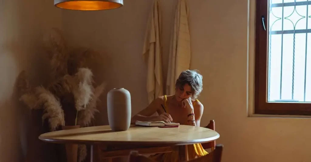 Woman writing in a journal at a peaceful table, reflecting near a window